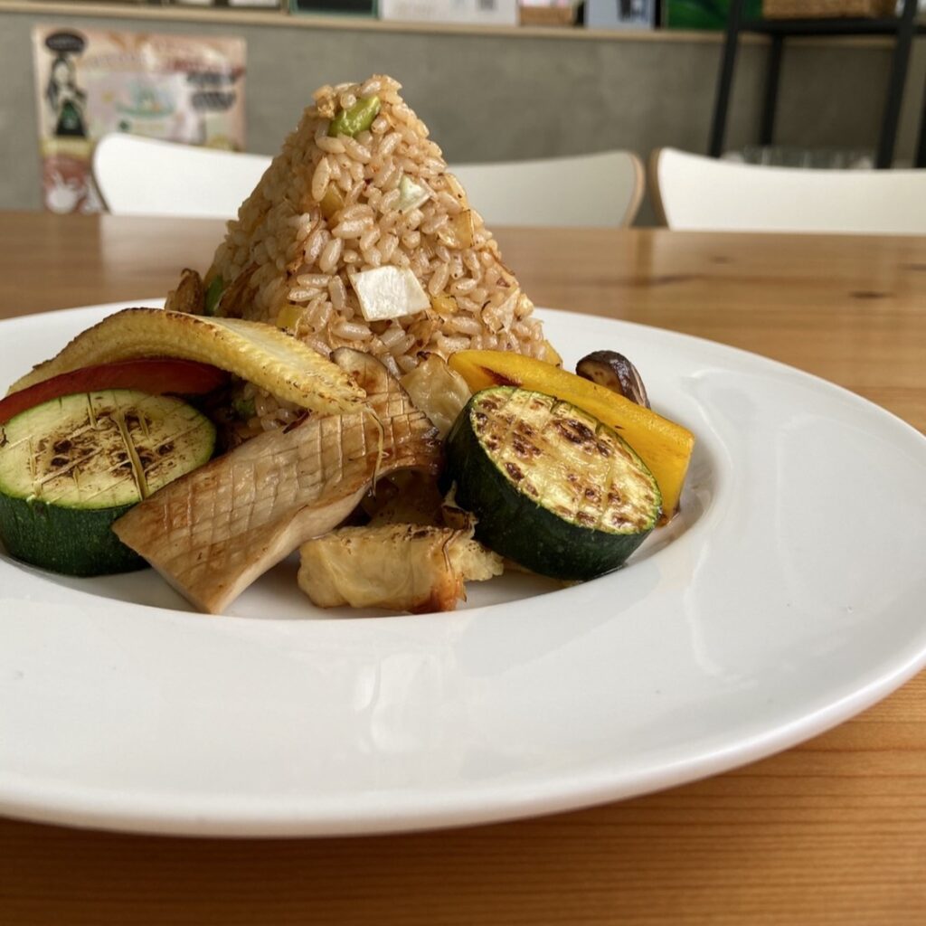 白色盤子裝著金字塔型的米食料理，包含櫛瓜、玉米筍、杏鮑菇